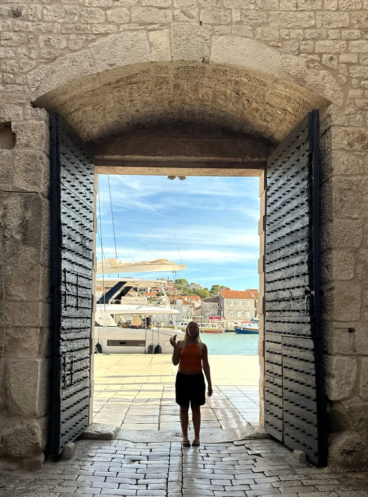 A girl eating rafioli at the entrance to the Old Town in Trogir with Riva in the background on a sunny day