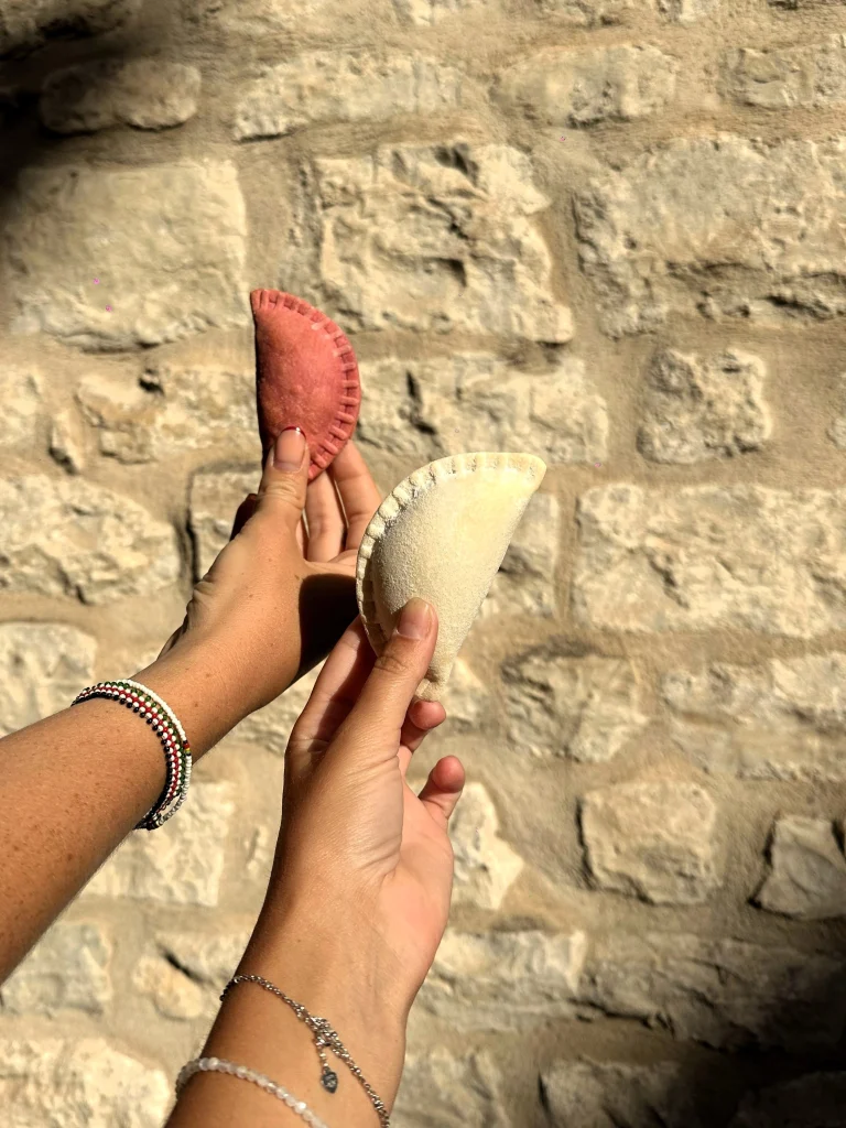 Two hands holding a rafioli each with cobblestone background at sunset