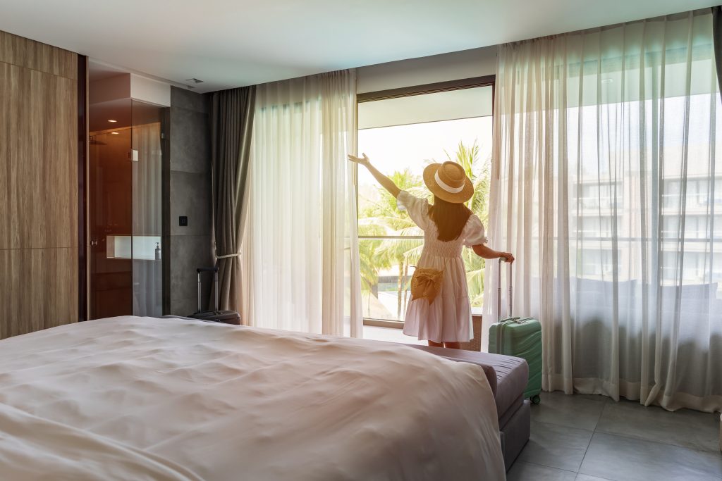A young woman looking out the window with excitement in a freshly checked-in hotel room